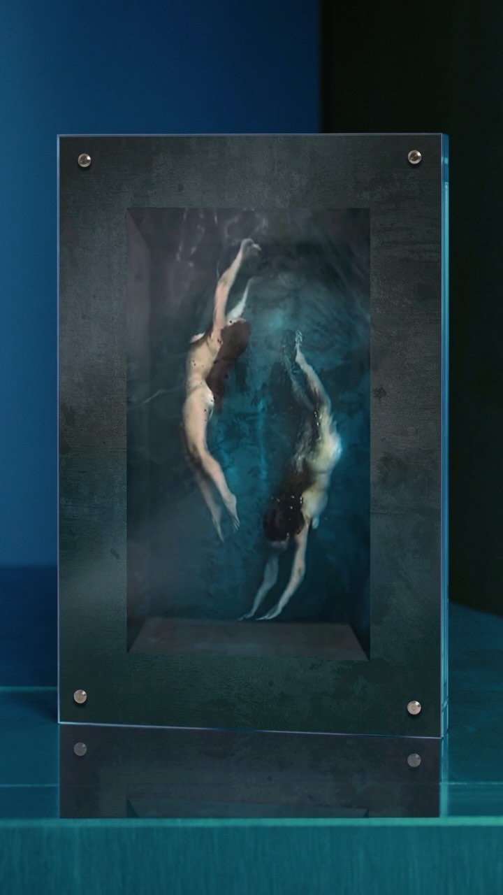 Two adult females appear to float in an abstract, surreal underwater scene depicted inside a dark-framed display object.