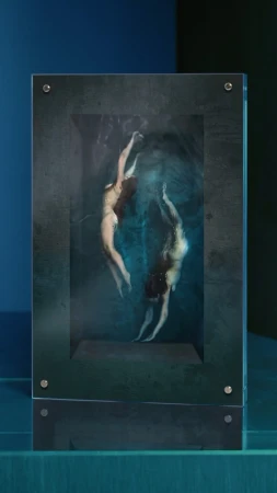 Two adult females appear to float in an abstract, surreal underwater scene depicted inside a dark-framed display object.