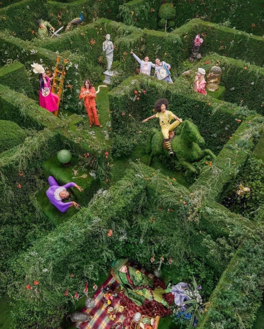 Aerial view of people posing in a garden maze featuring green hedges, topiary art, and whimsical costumes for a surreal fashion shoot.