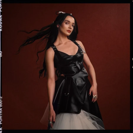 Portrait of a woman with long dark hair wearing a black leather corset top and white tulle skirt by Sam Cannon