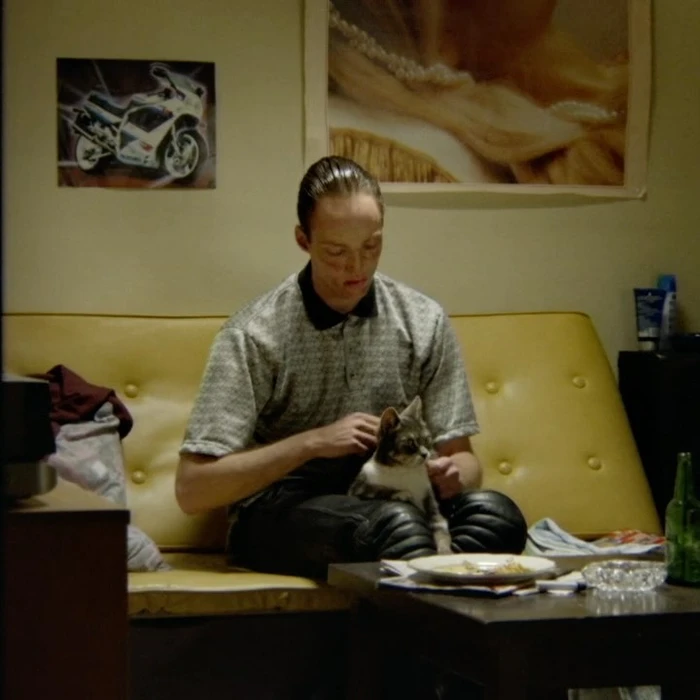 Man seated on a yellow sofa petting a small cat in a living room directed by Sam De Jong