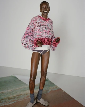 Woman in oversized knit sweater and socks poses on beach-themed paper in a studio with a white backdrop and soft, diffused lighting.