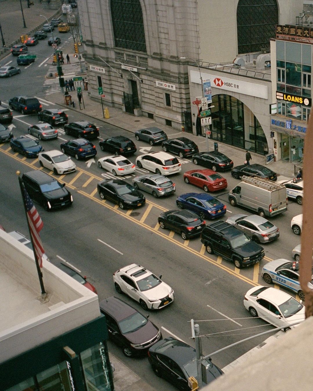Aerial view of a busy city street with multiple cars in daylight near buildings, showcasing urban traffic.