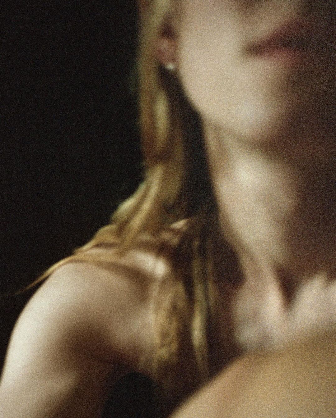 Close-up studio shot of a fair-skinned adult female with blonde hair partially visible, set against a dark background.