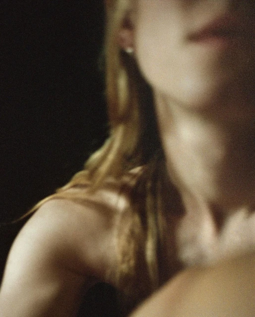 Close-up studio shot of a fair-skinned adult female with blonde hair partially visible, set against a dark background.