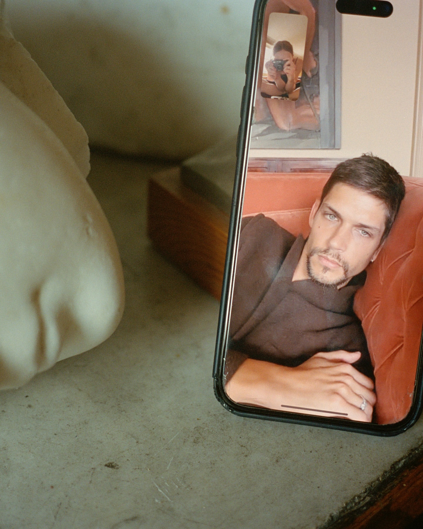 Man posing in cell phone reflection, captured on a table next to a sculpture, creating a modern, artistic image.