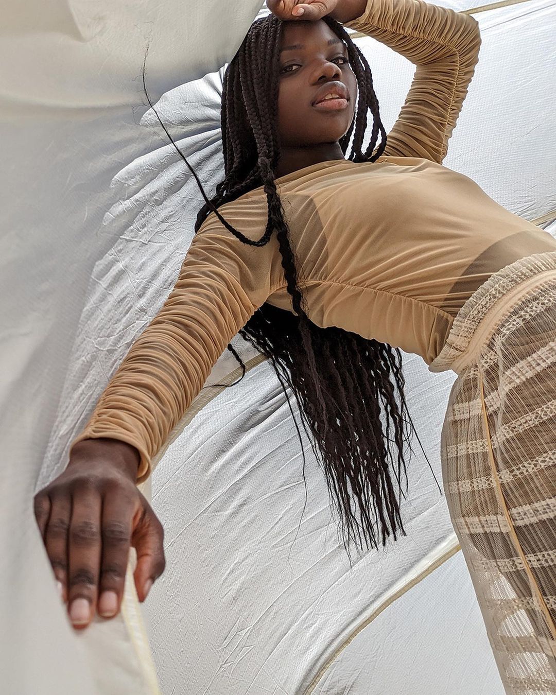 Adult woman in a sheer top and skirt poses in a low angle shot against a white background, showcasing fashion and style in a studio setting.
