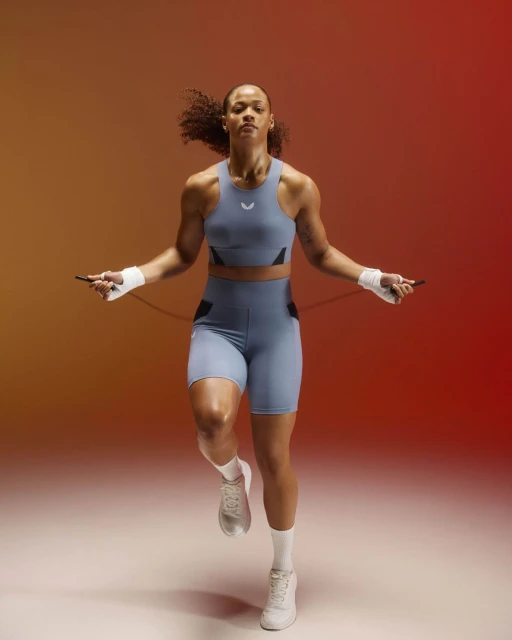 Athletic woman in sportswear jumps rope against a gradient background. The image captures a dynamic moment of fitness and athleticism.