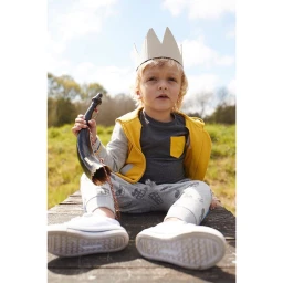 Young child wearing a paper crown and yellow vest sitting outdoors on a wooden dock holding a dark horn