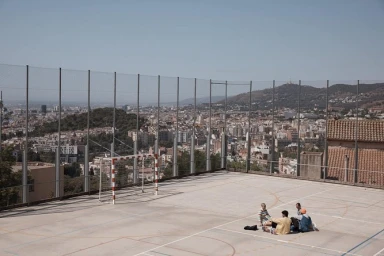 Four people sitting together on a concrete rooftop sports court overlooking a sprawling cityscape.