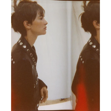 A brunette woman in a black leather jacket poses in profile view, duplicated in a shallow depth-of-field fashion photograph indoors.