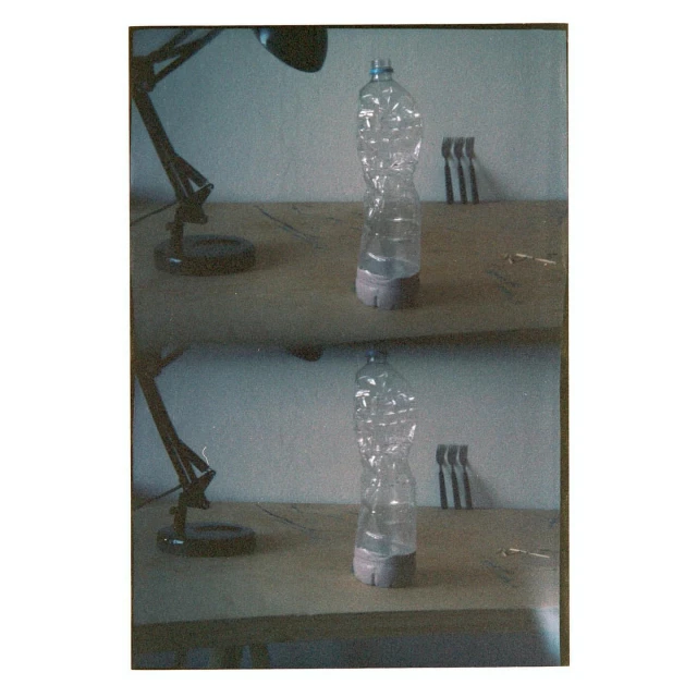 Still life featuring a distorted plastic water bottle on a wooden table, illuminated by a black desk lamp. Three metal objects in background.