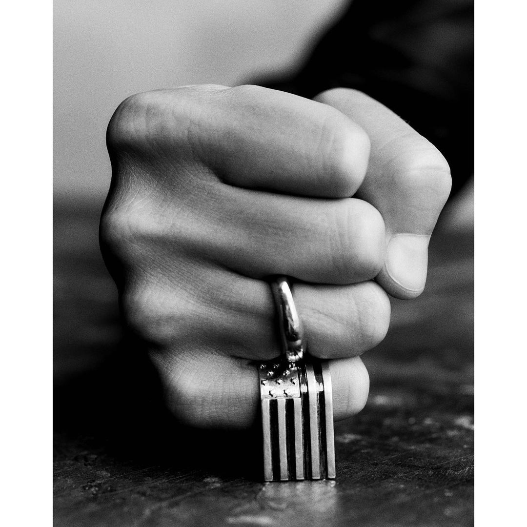 Close-up in black and white of a fist with a ring holding a small fork, showcasing hand details and the utensil's design.