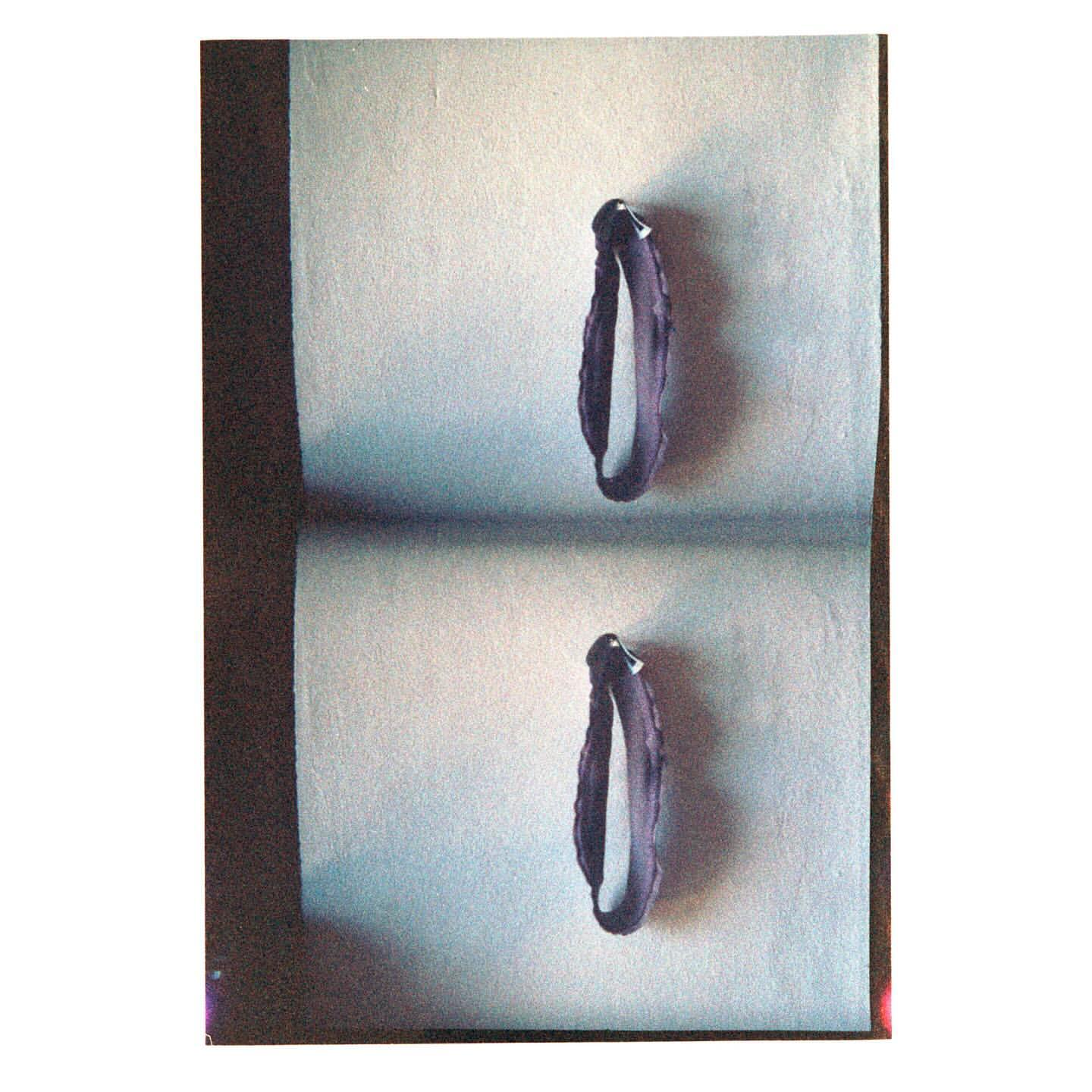 Still life studio shot of two violet bracelets on a gray surface with soft shadow, showcasing fashion accessories in a simple setting.