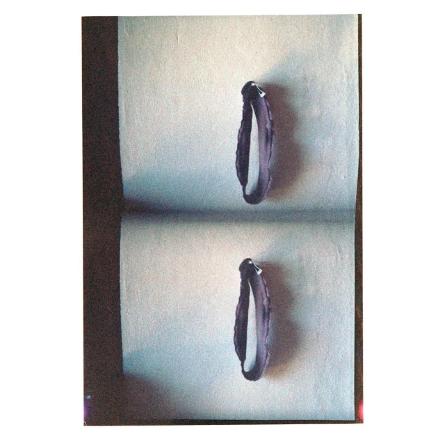 Still life studio shot of two violet bracelets on a gray surface with soft shadow, showcasing fashion accessories in a simple setting.