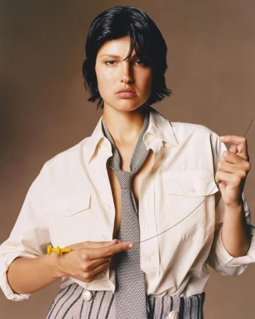 Portrait of a woman with dark hair in a white shirt and striped pants, holding a yellow syringe and a long needle in a studio.