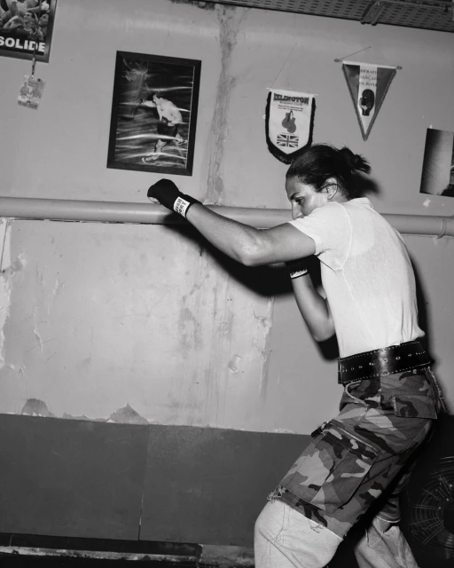 Monochrome image of a brunette male boxer in mid-punch in an indoor boxing gym, featuring faded posters and flags in the background.
