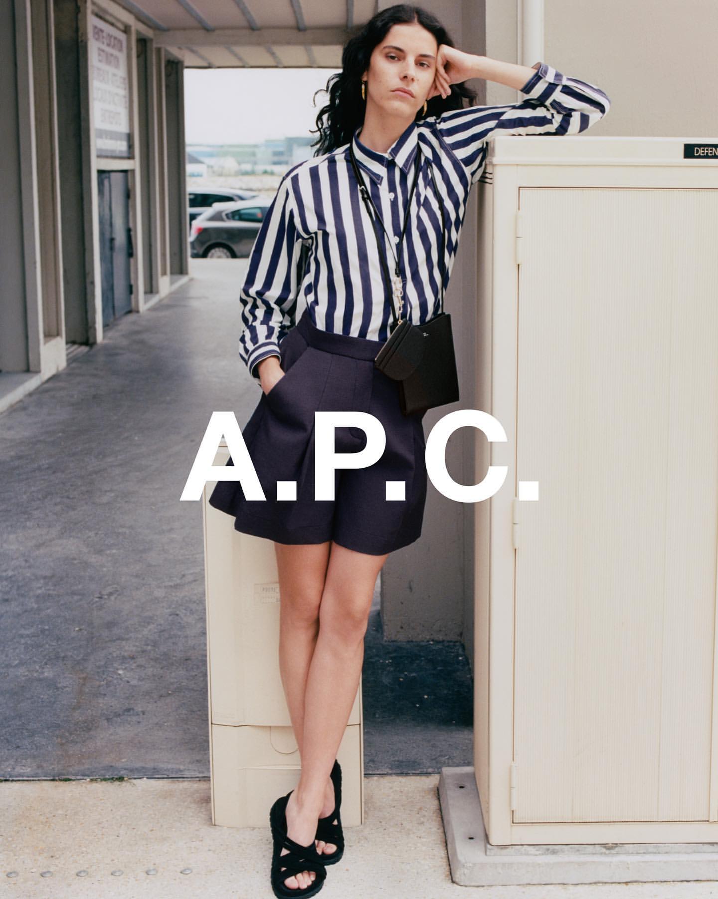 A woman in a striped shirt and shorts poses against a wall outdoors. The image highlights fashion and urban settings with a focus on style.
