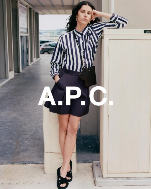 A woman in a striped shirt and shorts poses against a wall outdoors. The image highlights fashion and urban settings with a focus on style.