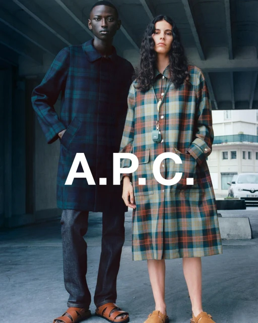 Two models in plaid coats stand against a concrete backdrop with a parked car; the A.P.C. logo is superimposed in the middle.