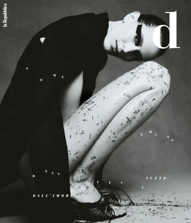 Monochrome fashion shot of a woman crouching with dark hair, a black jacket, and dark shoes, scattered leaf debris, and magazine text.