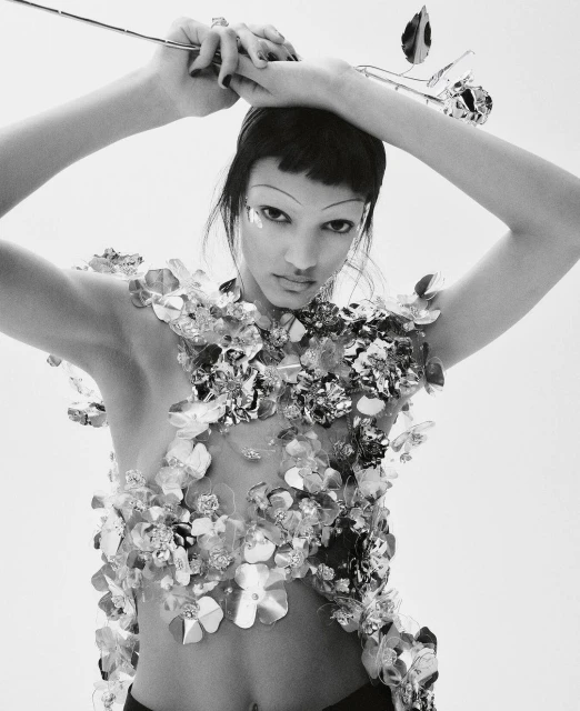 Black and white fashion portrait of a woman with short dark hair, wearing silver floral embellishments, holding a metallic rose.