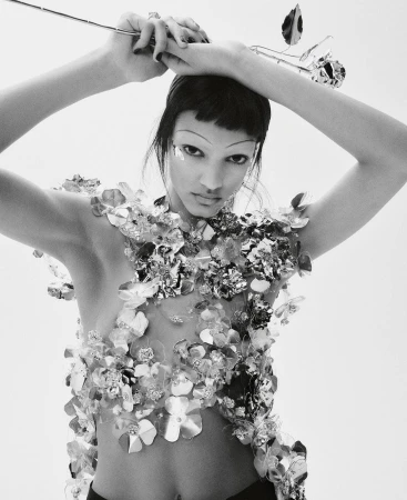 Black and white fashion portrait of a woman with short dark hair, wearing silver floral embellishments, holding a metallic rose.