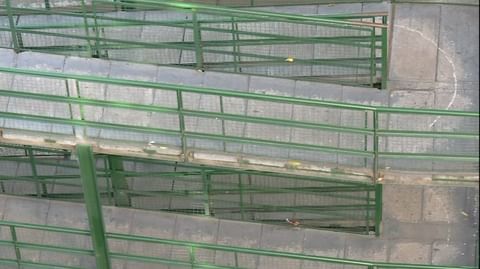 Elevated view of green metal stairs with mesh railings and concrete steps forming a tiered walkway, providing access to upper levels.