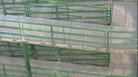 Elevated view of green metal stairs with mesh railings and concrete steps forming a tiered walkway, providing access to upper levels.