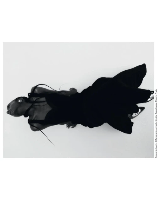 Top-down editorial fashion shot: Woman in a black gown and silver heels lies on a white surface with soft studio lighting.  