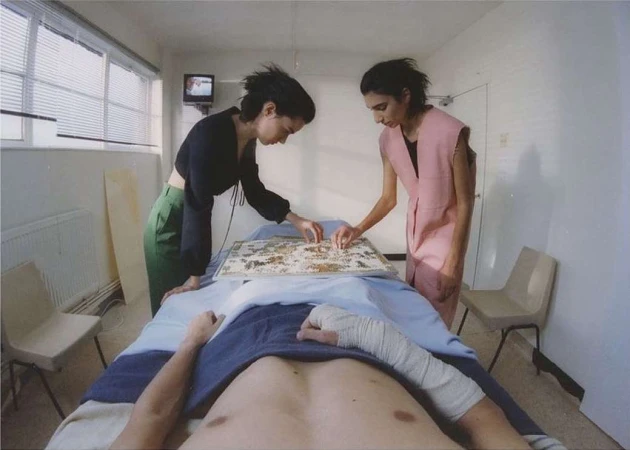 Two women completing a puzzle for a man lying on an examination table in a clinical room. Patient is partially covered with a blanket.