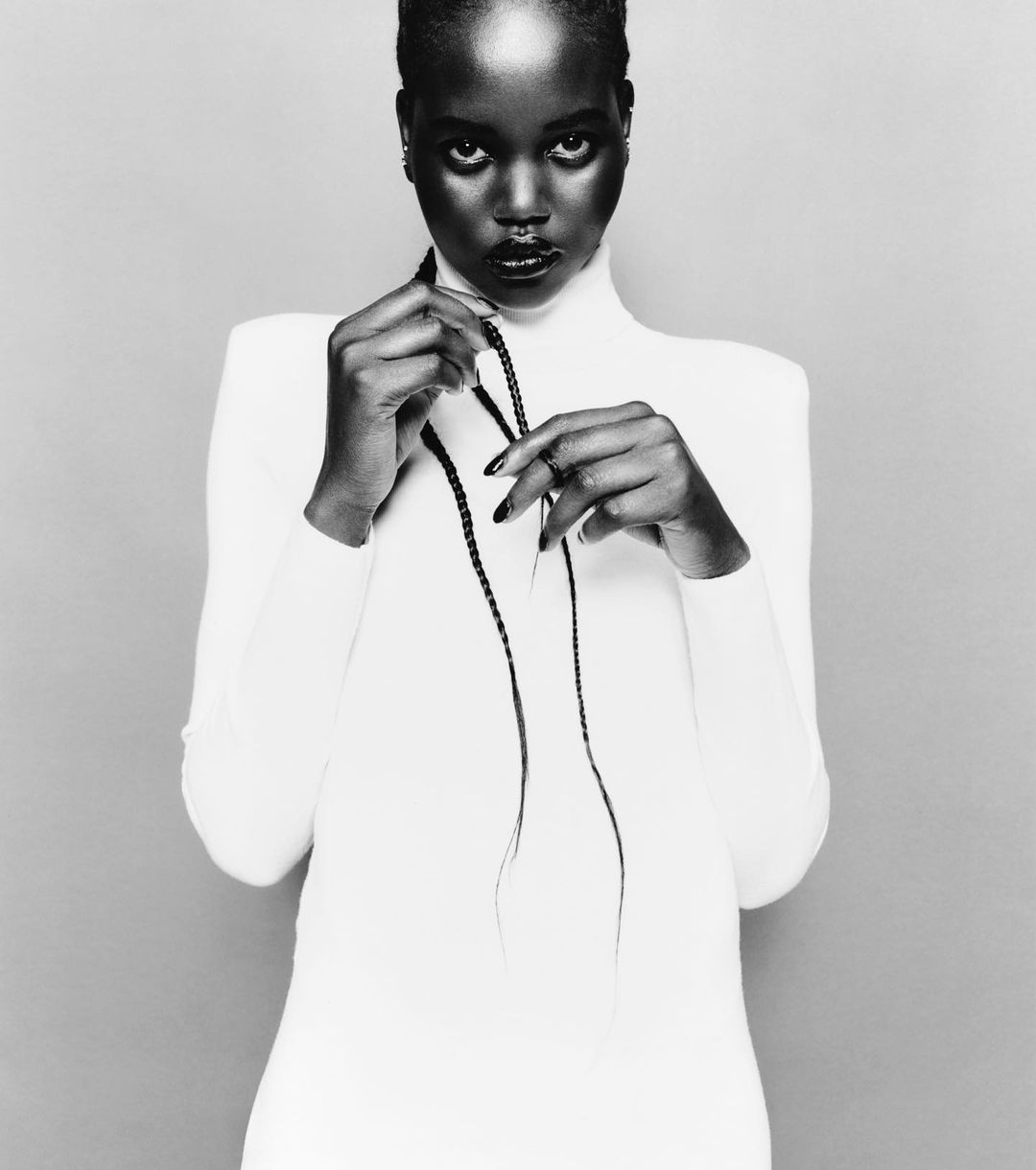 Black and white studio portrait of a woman wearing a white turtleneck top holding braided hair by photographer Sam Rock