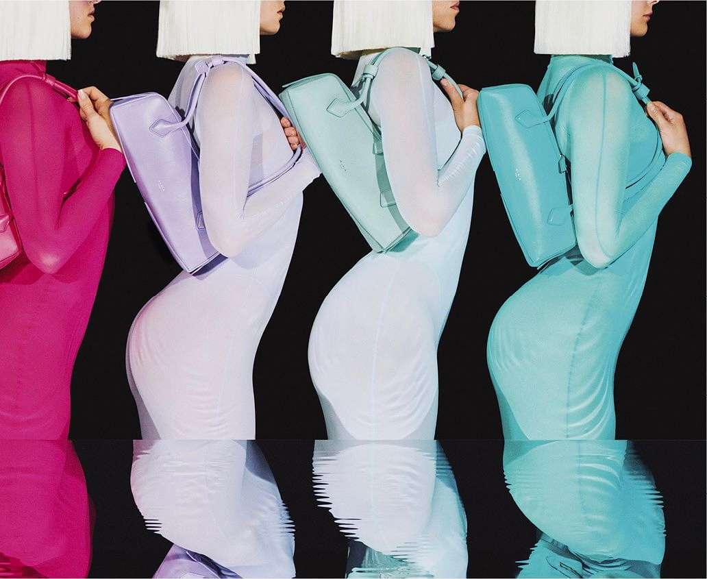Fashion shot of four women with white wigs wearing pink, lavender, green, and teal sheer dresses, each holding a matching handbag.