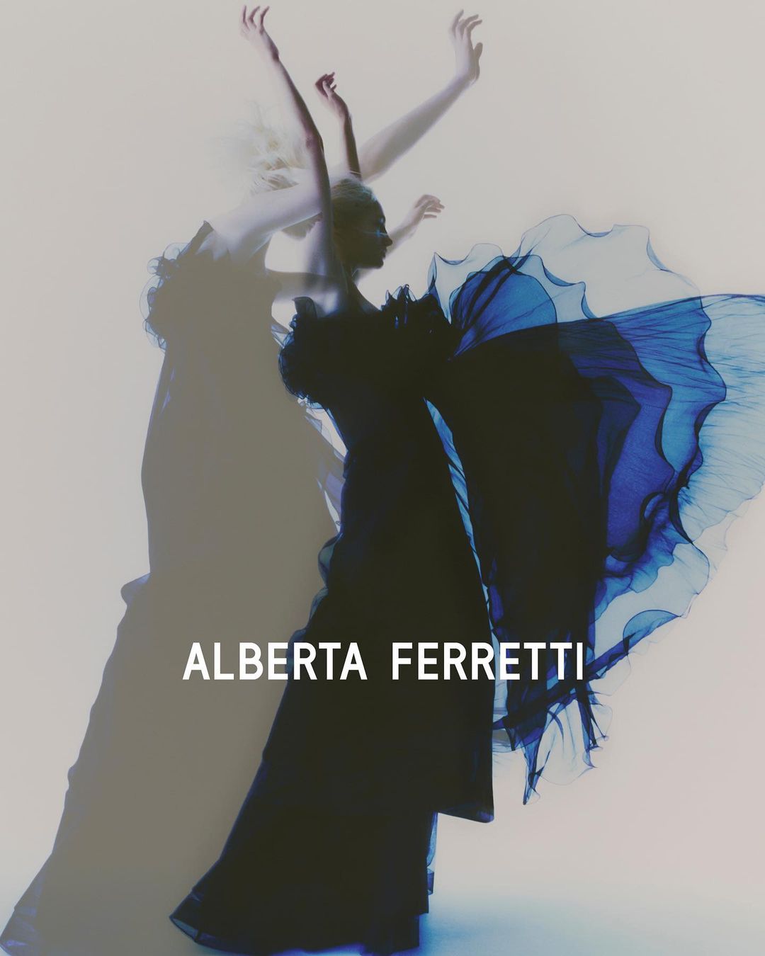 Fashion shot featuring a model in an elegant blue gown, with soft lighting and a blurred silhouette effect against a white backdrop.