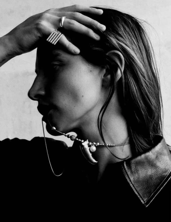 Close-up monochrome portrait of a model with long hair wearing statement rings and a charm necklace by photographer Sam Rock
