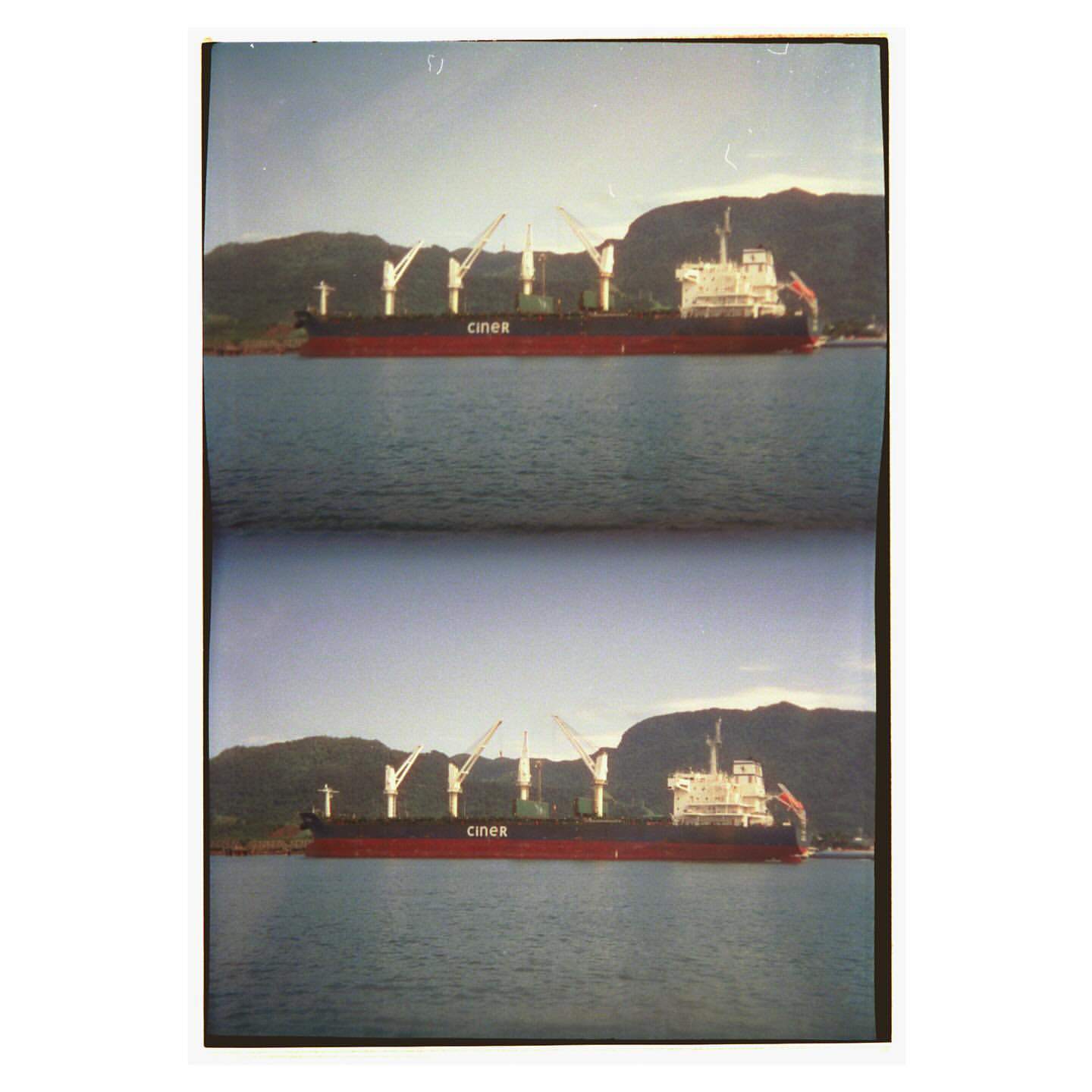 Cargo ship with cranes in harbor near green mountains under a clear sky. Commercial shipping transport and coastal landscape. 