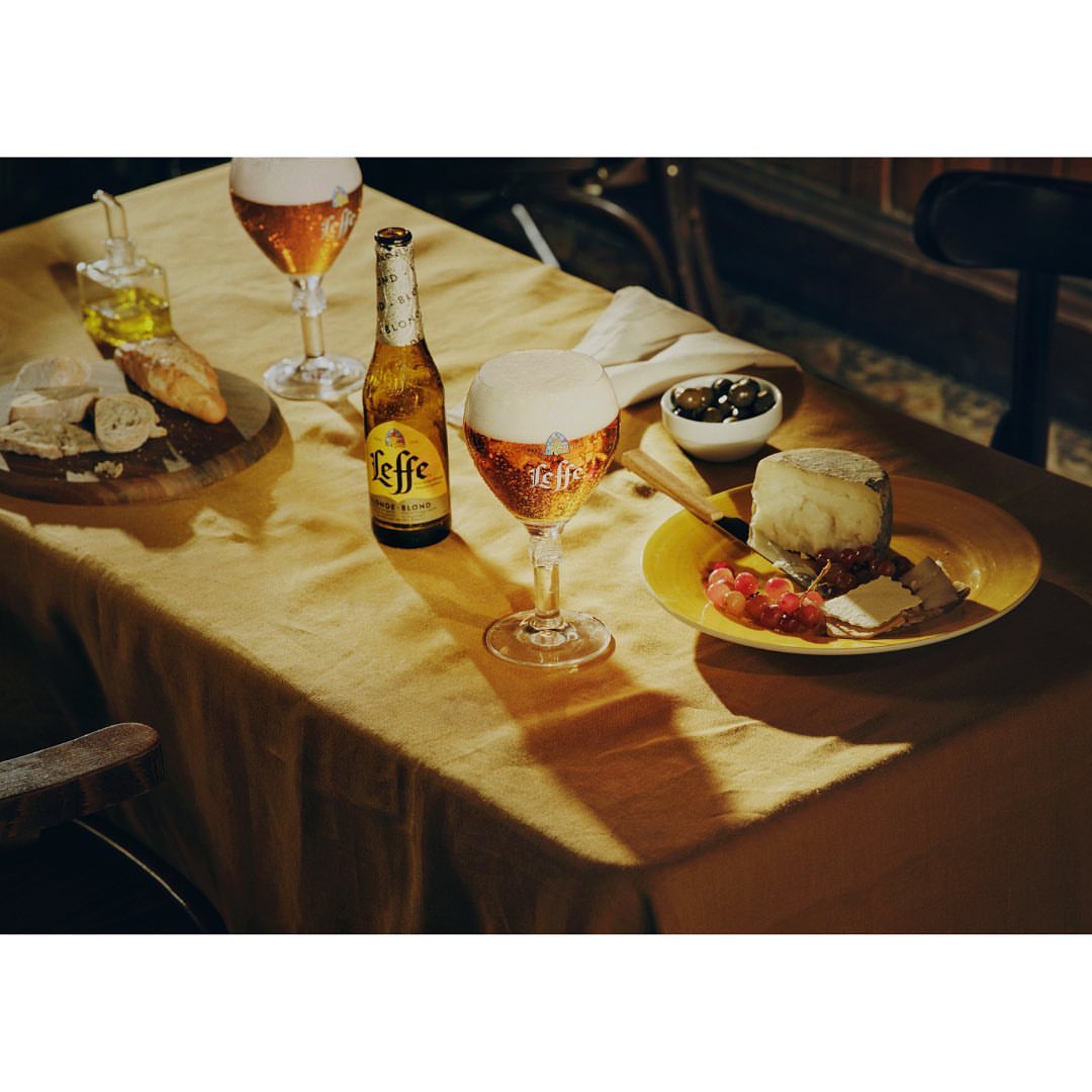 Still life shot of two Leffe beer glasses and one bottle arranged on a table with cheese, crackers, and grapes, creating a social atmosphere.