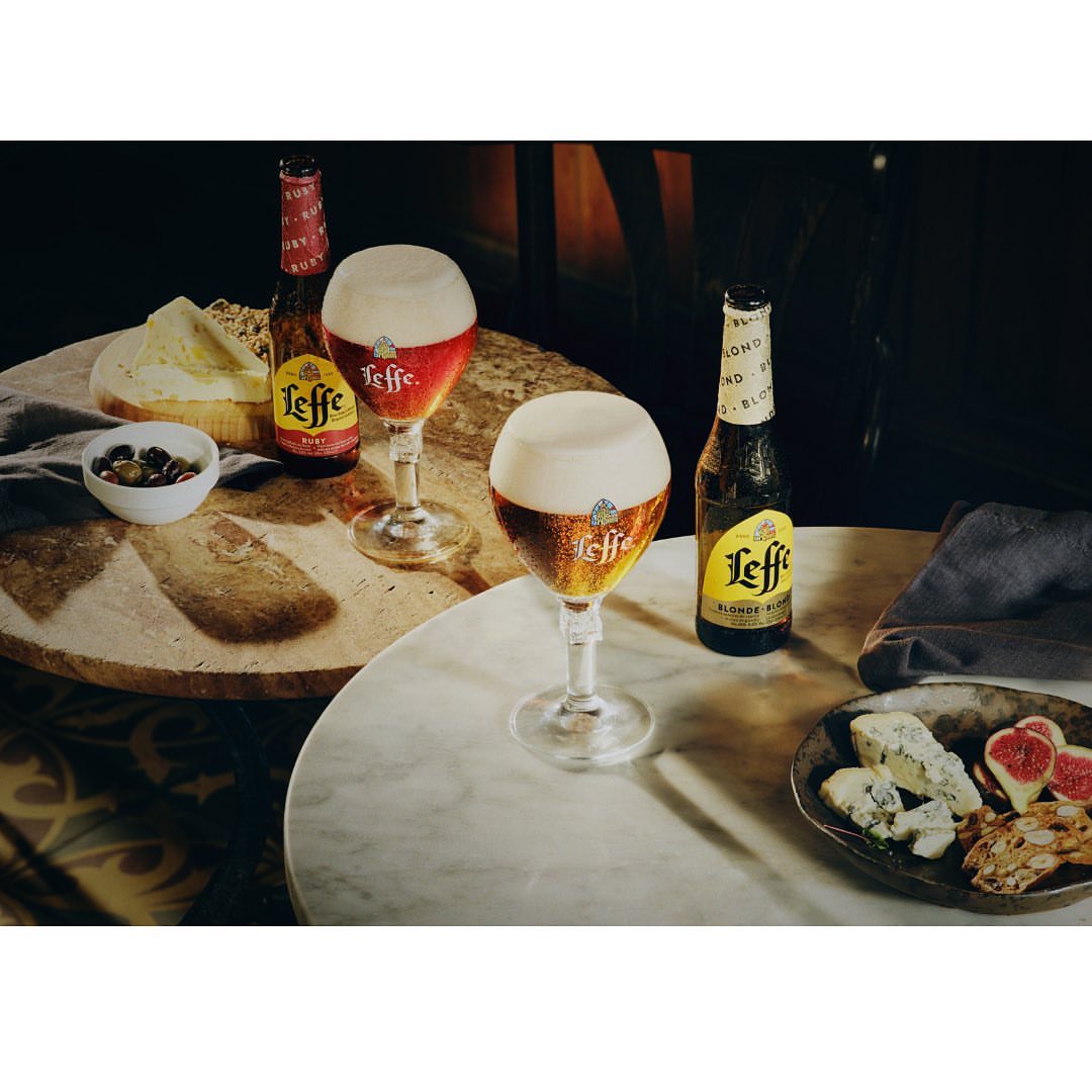 Two glasses of Leffe beer next to bottles and cheese platters on marble tables, creating an inviting and refreshing beverage scene.