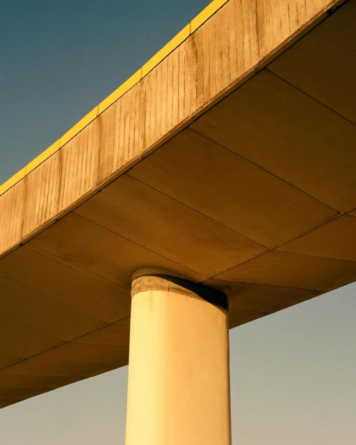 Low-angle shot of a concrete overpass support with a yellow accent under a light blue sky, architecture with structural concrete.