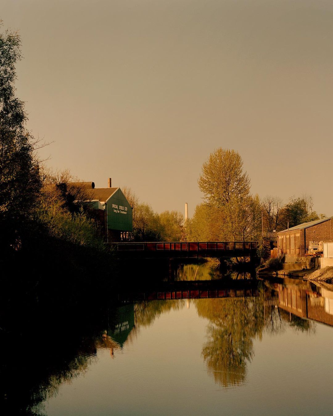 Scenic view of a river with a bridge and reflective building in the background, captured under a cloudy sky at dusk or dawn.
