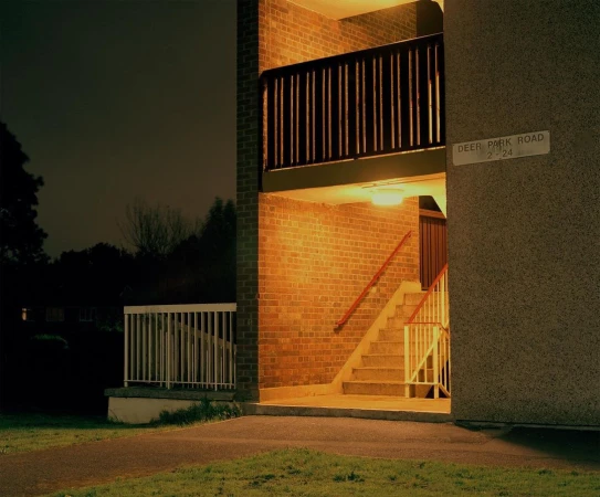 Exterior of an illuminated brick apartment building at night with stairs leading up, featuring warm lighting and architectural details.