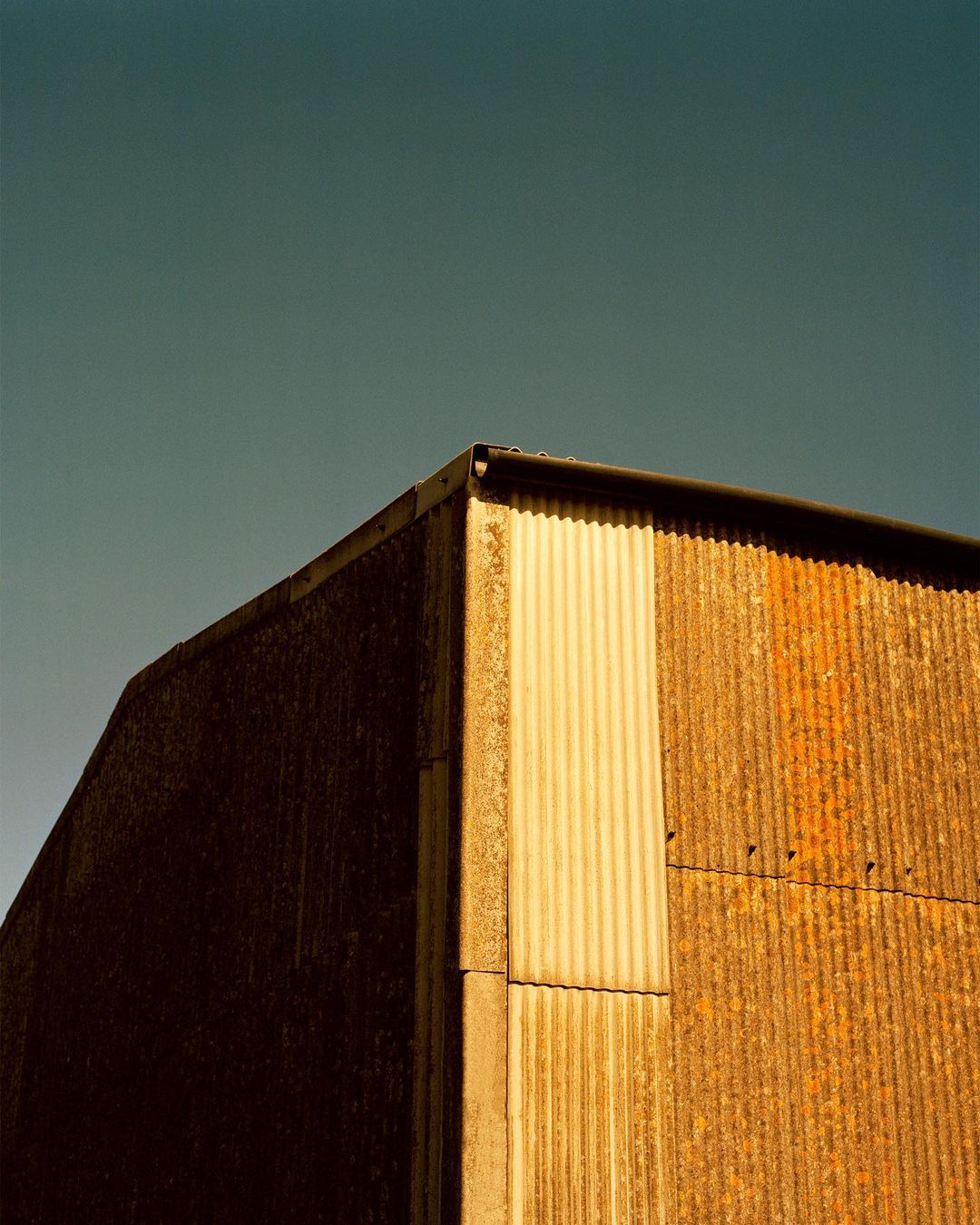 Low-angle shot of a rustic building corner under a clear sky, featuring weathered metal cladding and architectural details.