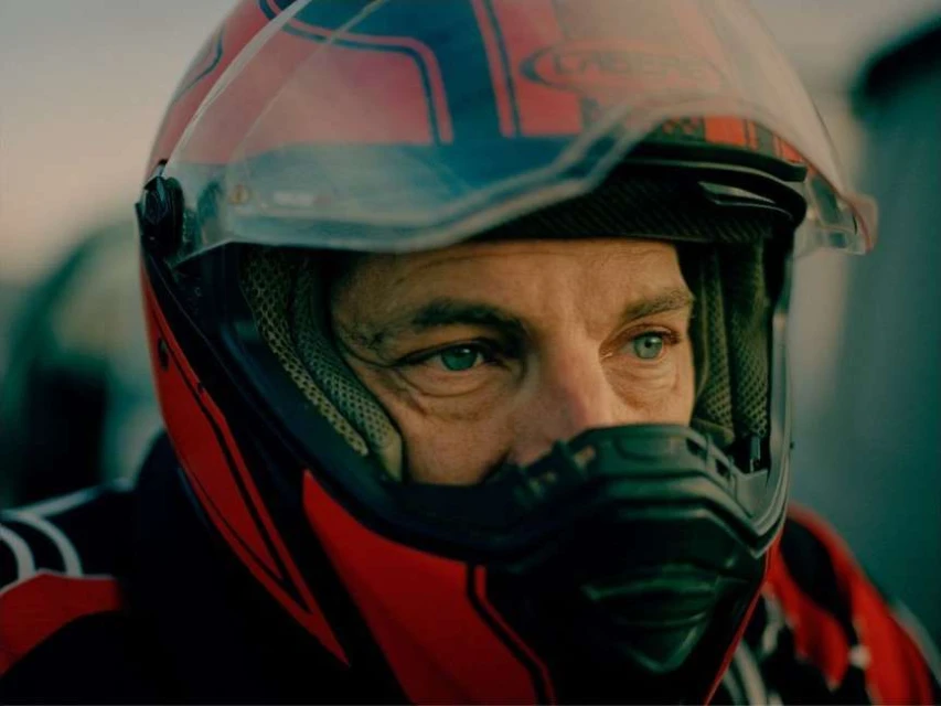 Adult male wearing a red and black motorcycle helmet looks off to the side in a medium shot. 