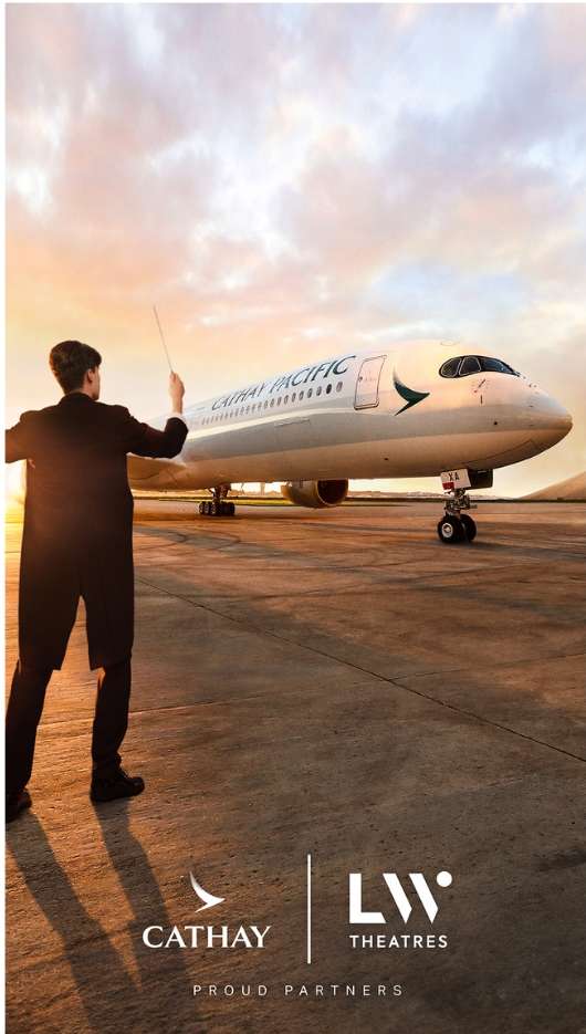 Airplane on the tarmac at sunset with a person in a suit standing in the foreground, near airport buildings and a warm-colored sky.