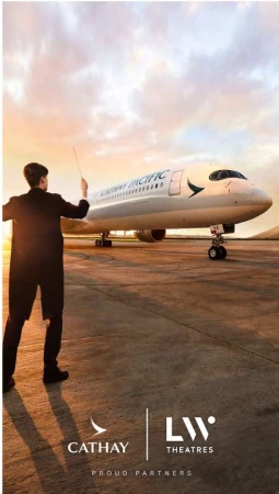 Airplane on the tarmac at sunset with a person in a suit standing in the foreground, near airport buildings and a warm-colored sky.