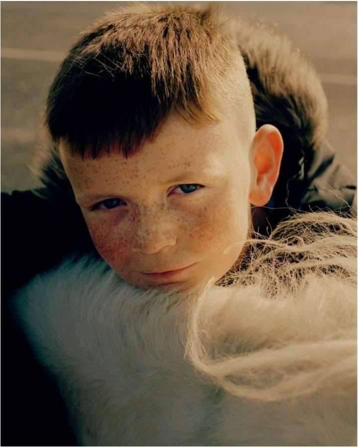 Close-up portrait of a young boy with freckles resting his chin on a white horse mane, photographed by Sam Wright.