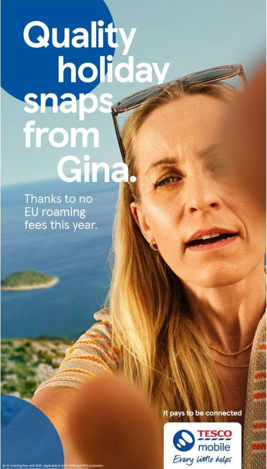 An adult woman with long blonde hair is taking a selfie on vacation against a coastal backdrop for a Tesco Mobile advertisement with clear text.