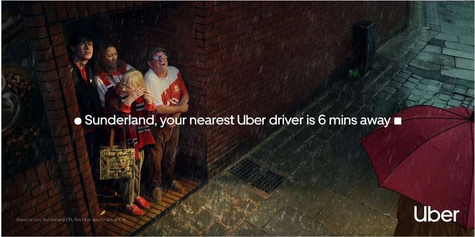 A group of people standing under the rain near a brick building, featuring an Uber advertisement with an umbrella and the Uber logo.