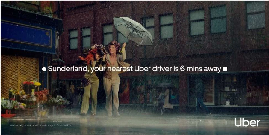 Two women walk in the rain under an umbrella in a city street, captured in a medium shot highlighting the urban weather.