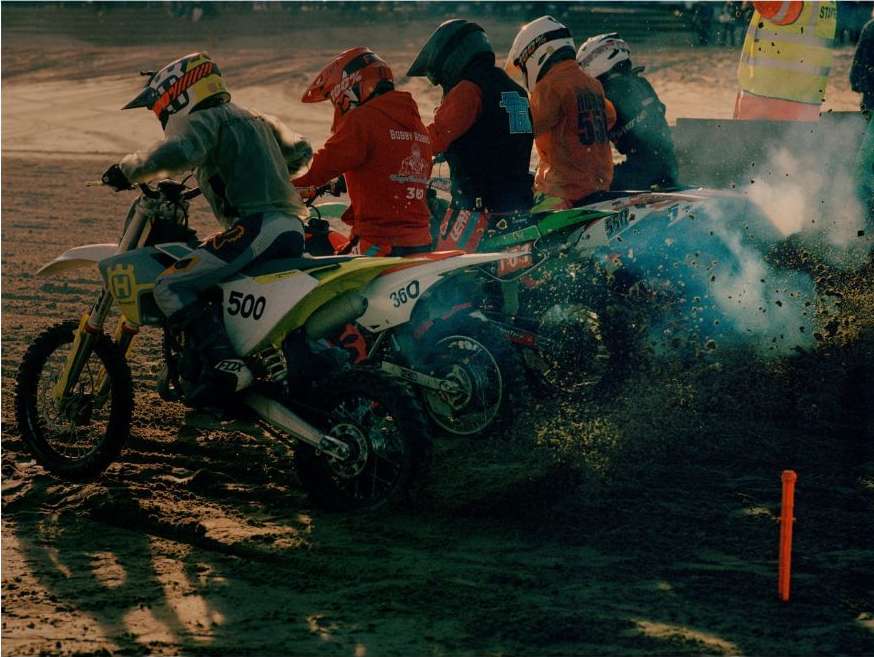 A dynamic outdoor shot showcases a group of motocross racers speeding down a dirt track on their bikes, kicking up dirt and smoke.